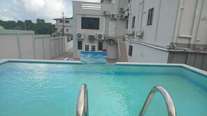 Una piscina con escaleras metálicas, rodeada por un edificio con unidades de aire acondicionado y una puerta.