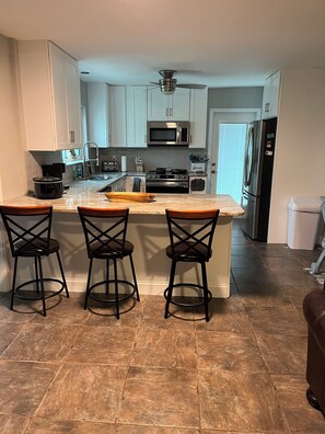 Una cocina moderna con armarios blancos, una isla central con taburetes de bar, microondas, estufa y refrigerador.