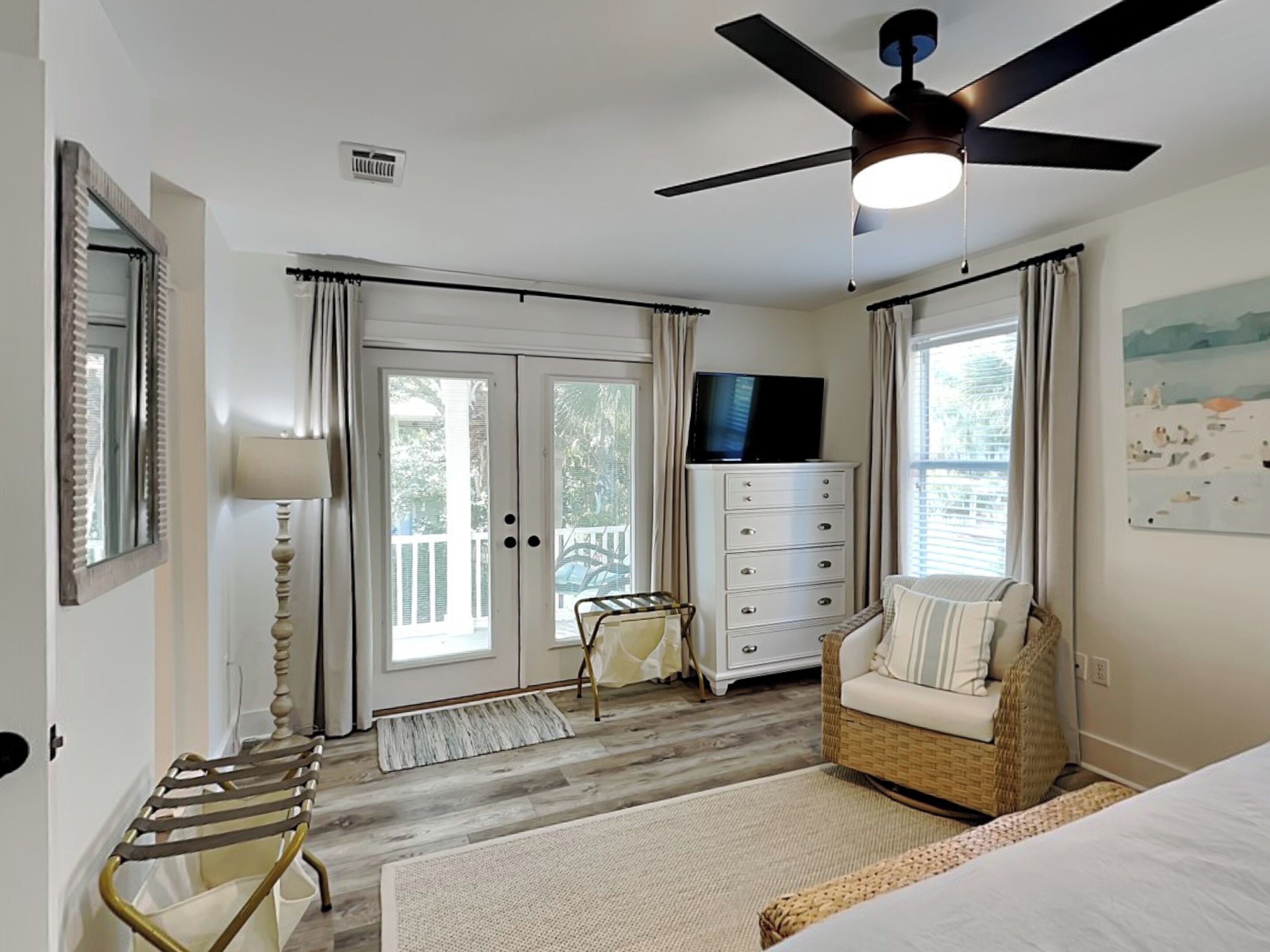 A bedroom with a ceiling fan, a TV on a dresser, a wicker chair, and a bed.