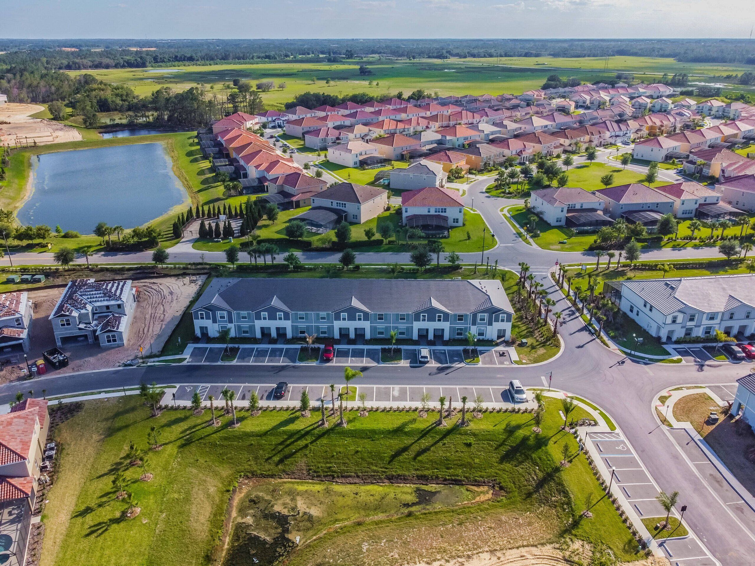 Vista aérea de una zona residencial con varias casas, un edificio grande con estacionamiento y una masa de agua.