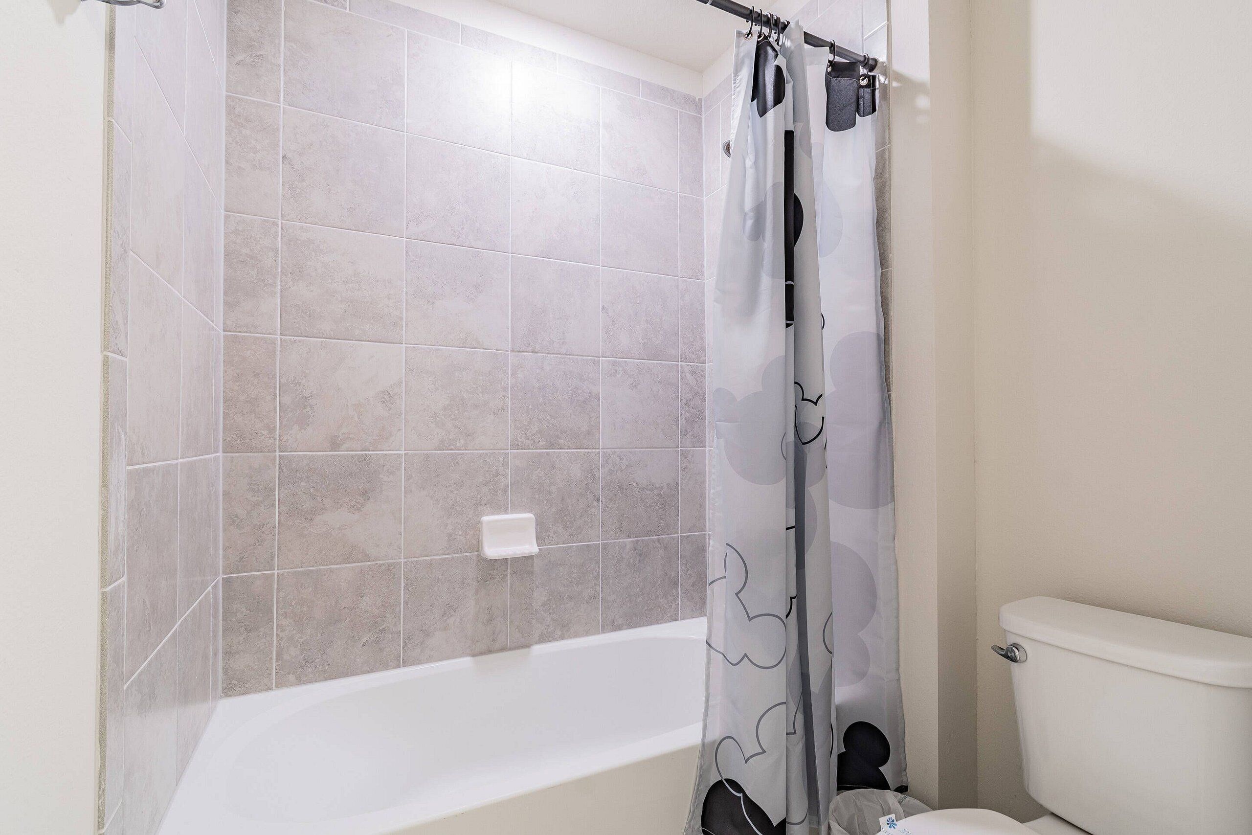 A bathroom with a bathtub, a toilet, and a shower curtain with a Mickey Mouse design.