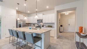 A modern kitchen with a large island, bar stools, stainless steel appliances, and pendant lighting. - Disney 5BR Villa w/ Pool Solterra Resort (Davenport)