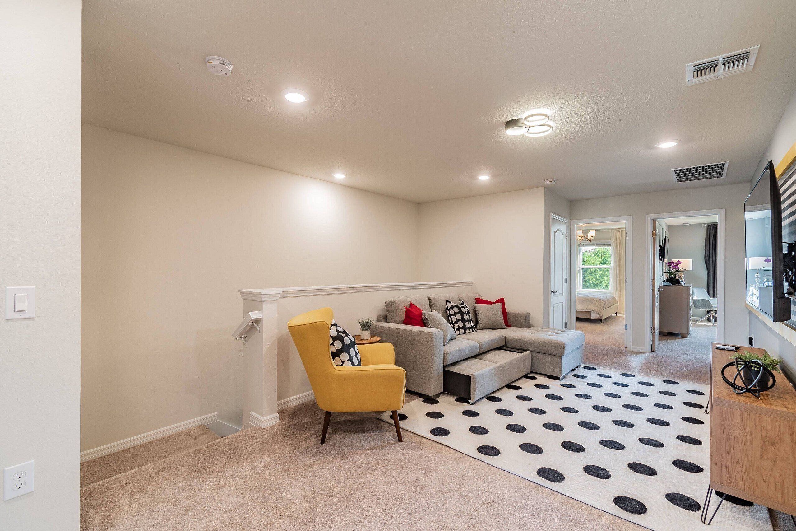 A modern living room with a sectional sofa, a yellow armchair, and a polka dot rug.
