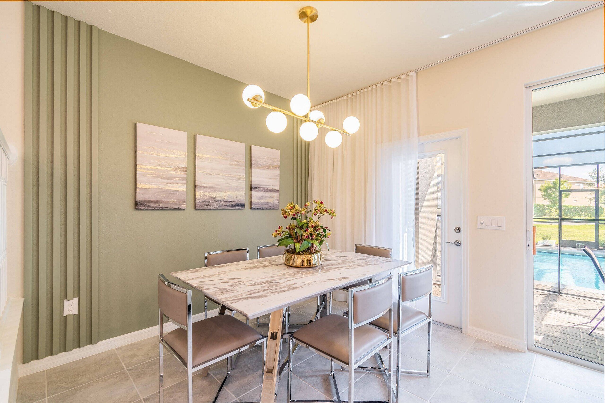 A dining area with a marble table, six chairs, a chandelier, and a view of a swimming pool through a glass door.