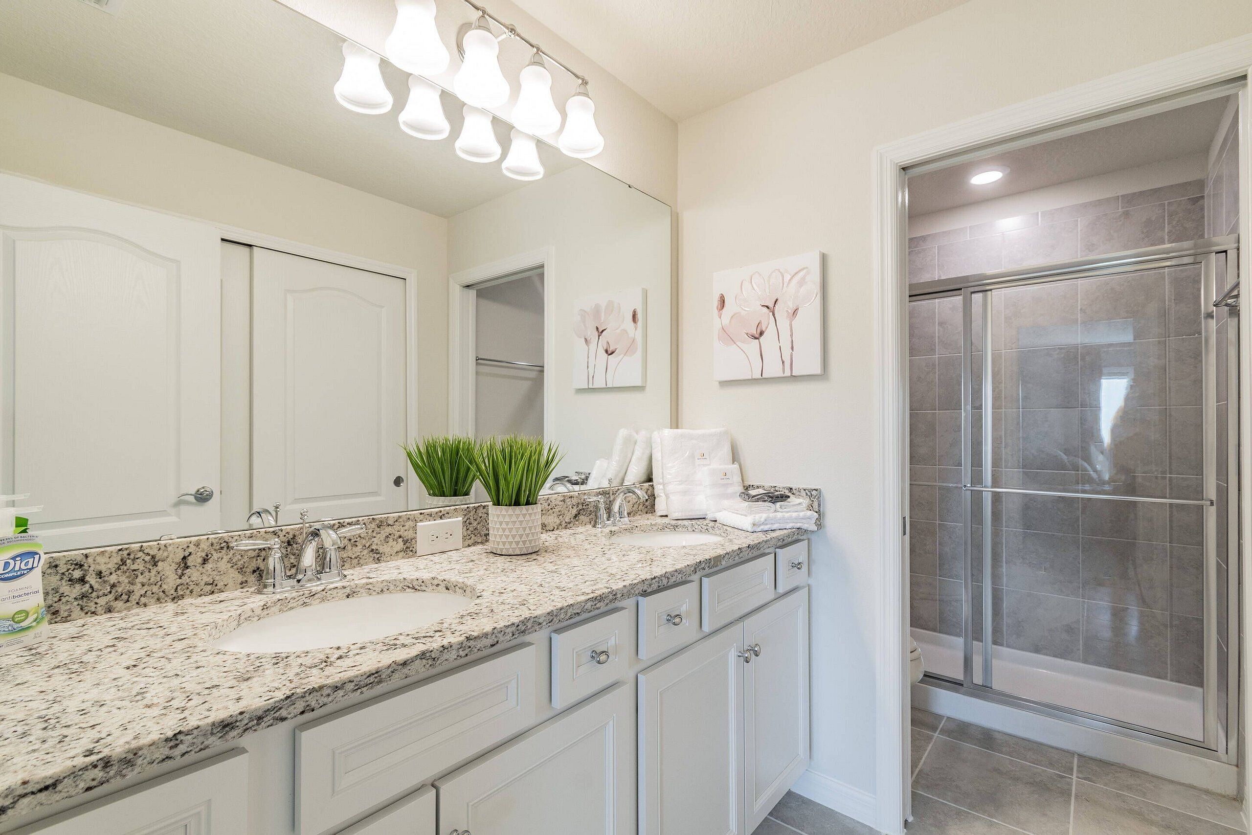 A bathroom with a granite countertop, a sink, a mirror, a shower enclosure, and wall-mounted lights.