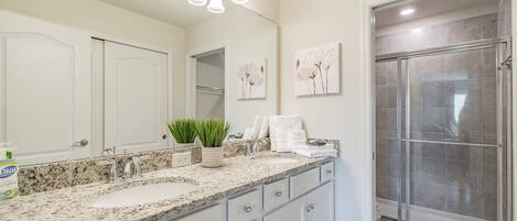 A bathroom with a granite countertop, a sink, a mirror, a shower enclosure, and wall-mounted lights.