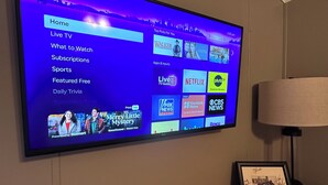 En platt-TV som är monterad på en vägg och visar ett Roku-användargränssnitt med olika alternativ för strömmande innehåll.