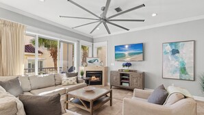 A living room with a fireplace, a ceiling fan, and a large window with curtains. - Games, Elevator, Ensuites, Pool, Bikes, Elevator (Destin)