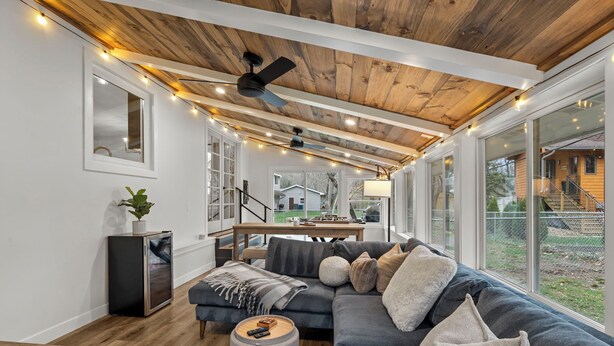 A modern living room with a wooden ceiling, large windows, and a grey sectional sofa.