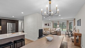 A modern kitchen with a central island, a dining area with a large table, and a living room with a sofa and a TV.