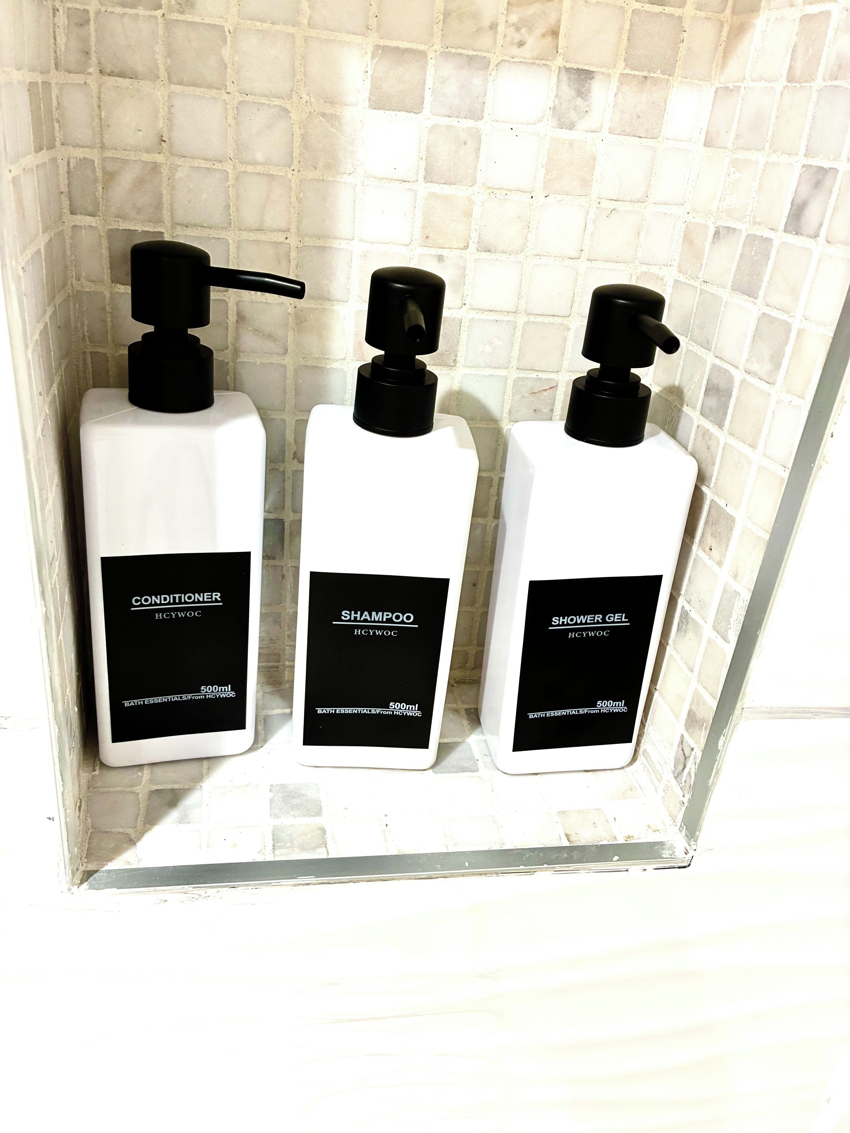 Tre flaconi di articoli da bagno su un muro piastrellato.