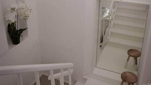 Un escalier avec des rampes blanches et une main courante en bois, menant à un palier avec un mur blanc et un pot de fleurs.