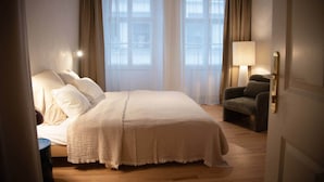 Une chambre d’hôtel avec un grand lit, une chaise, une lampe et une fenêtre avec des rideaux.