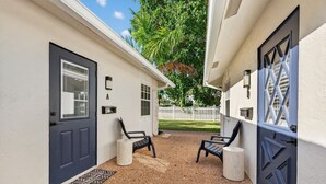 A covered outdoor area with two doors, a white picket fence, and a palm tree in the background. - The Tide: 2 Miles to Atlantic Ave - Walk to Beach (Delray Beach)