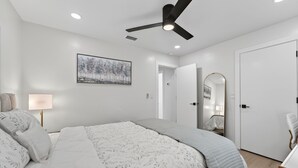 A bedroom with a bed, a ceiling fan, a wall-mounted lamp, a framed picture, and a door leading to another room. - The Tide: 2 Miles to Atlantic Ave - Walk to Beach (Delray Beach)