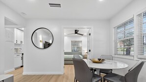 A modern kitchen with white cabinets, a round mirror, and a dining area with a white table and chairs. - The Tide: 2 Miles to Atlantic Ave - Walk to Beach (Delray Beach)