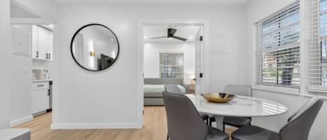 A modern kitchen with white cabinets, a round mirror, and a dining area with a white table and chairs.