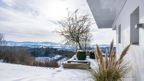 A modern building with a snow-covered landscape, a clear sky, and distant mountains. - Apartment “Himmelweit” with Mountain Views, Private Terrace and Wi-Fi (Freyung)