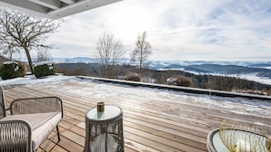 A wooden deck with wicker furniture, a glass table, and a candle holder. - Apartment “Himmelweit” with Mountain Views, Private Terrace and Wi-Fi (Freyung)