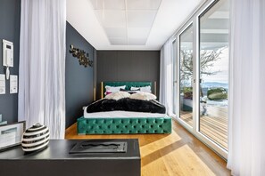 Ein modernes Schlafzimmer mit einem großen Bett, einem Schreibtisch mit einer Vase und Blick ins Freie.
