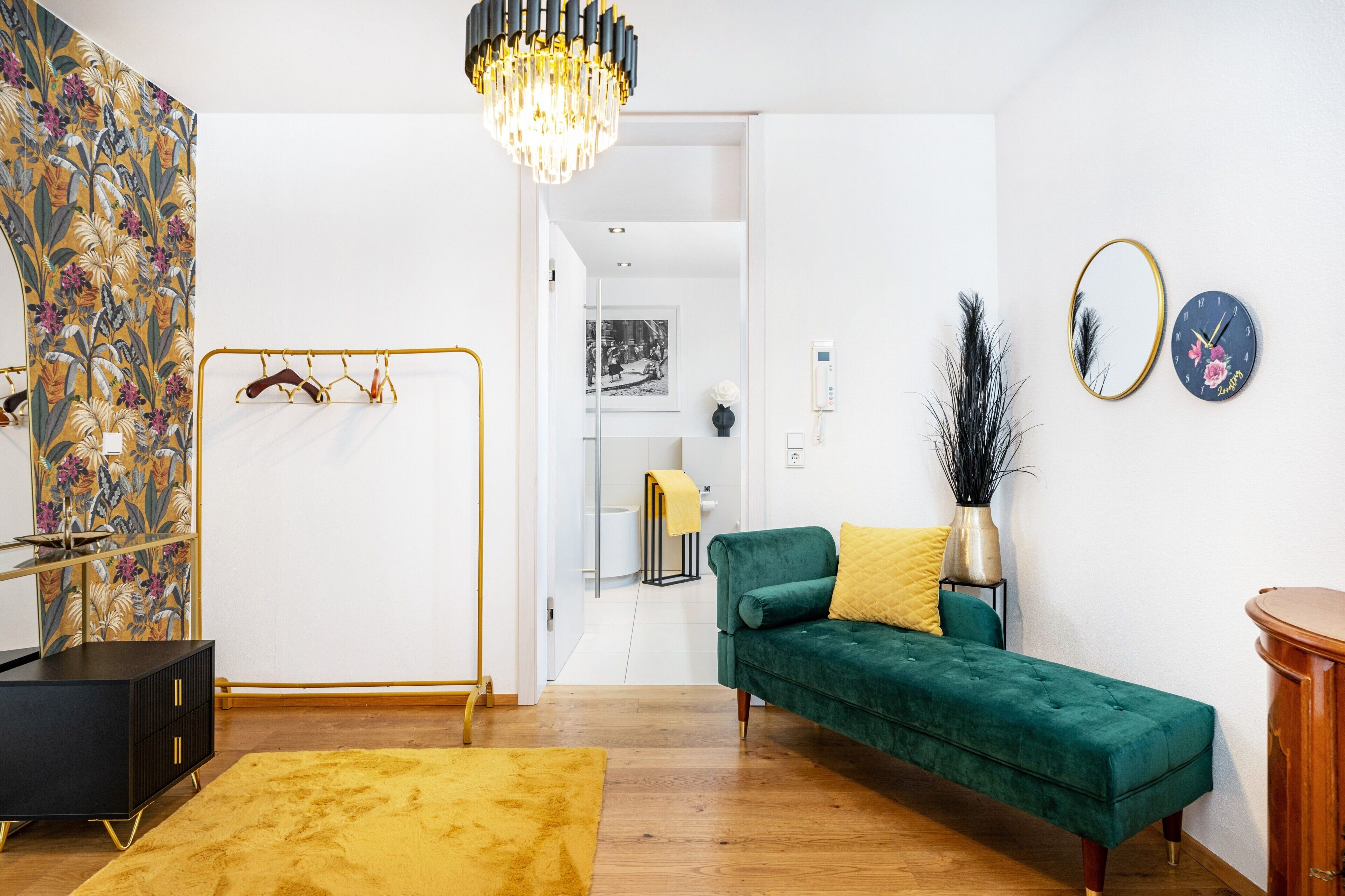 En moderne stue med en grøn sofa, en gul måtte, et sort skab og en lysekrone.