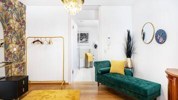En moderne stue med en grøn sofa, en gul måtte, et sort skab og en lysekrone.