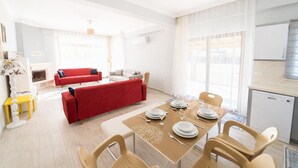A modern living room with a red sofa, a dining table set for four, and a kitchen area with a dishwasher.
