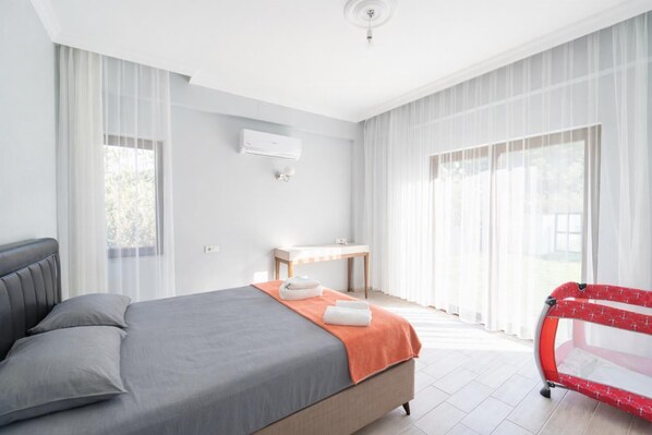 Une chambre à coucher comprenant un lit, une table de chevet, un appareil de climatisation et une fenêtre avec des rideaux.