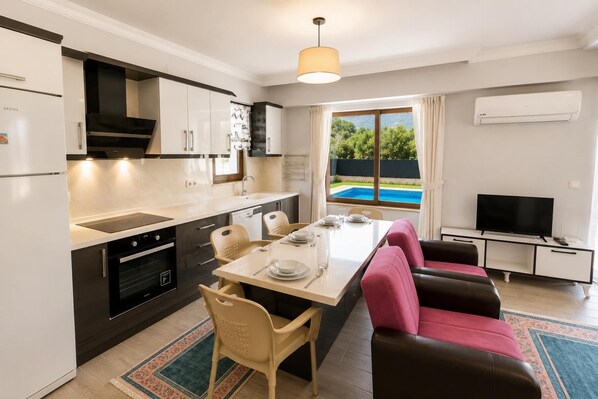 A modern kitchen with a dining area, a TV, and a view of a swimming pool. - Villa Larisa - Two Bedroom Villa, Sleeps 4 (Mergenli)