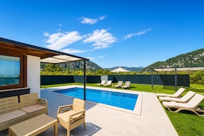 A pool area with lounge chairs, a covered seating area, and a view of mountains.