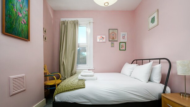 Een slaapkamer met een bed, een stoel, een raam met gordijnen en een kunstwerk aan de muur.