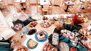 A dining area with multiple tables and chairs, a variety of food items displayed on tables, and a view of the outdoors through large windows. - Hotel Lo Smeraldo - Oasi degli Ulivi (Ventotene)