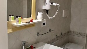 A bathroom with a white sink, two toilets, a mirror, and a hairdryer on a shelf. - Hotel Lo Smeraldo - Oasi degli Ulivi (Ventotene)