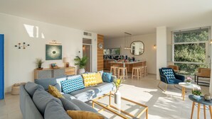 A modern living room with a sofa, coffee table, and chairs. There is a kitchen area with a dining table and chairs. - Casa Chiara 6+2, Emma Villas (Sori)