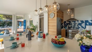 A modern kitchen with a central island, a clock, and a view of the outdoors. - Casa Chiara 6+2, Emma Villas (Sori)