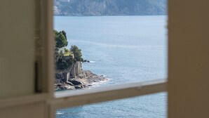 A view from a room with a window overlooking a body of water, a distant hill, and a lighthouse. - Casa Chiara 6+2, Emma Villas (Sori)