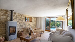 Una sala de estar acogedora con una pared de piedra, una chimenea, un sofá, una mesa de centro y vistas a una piscina a través de amplios ventanales.