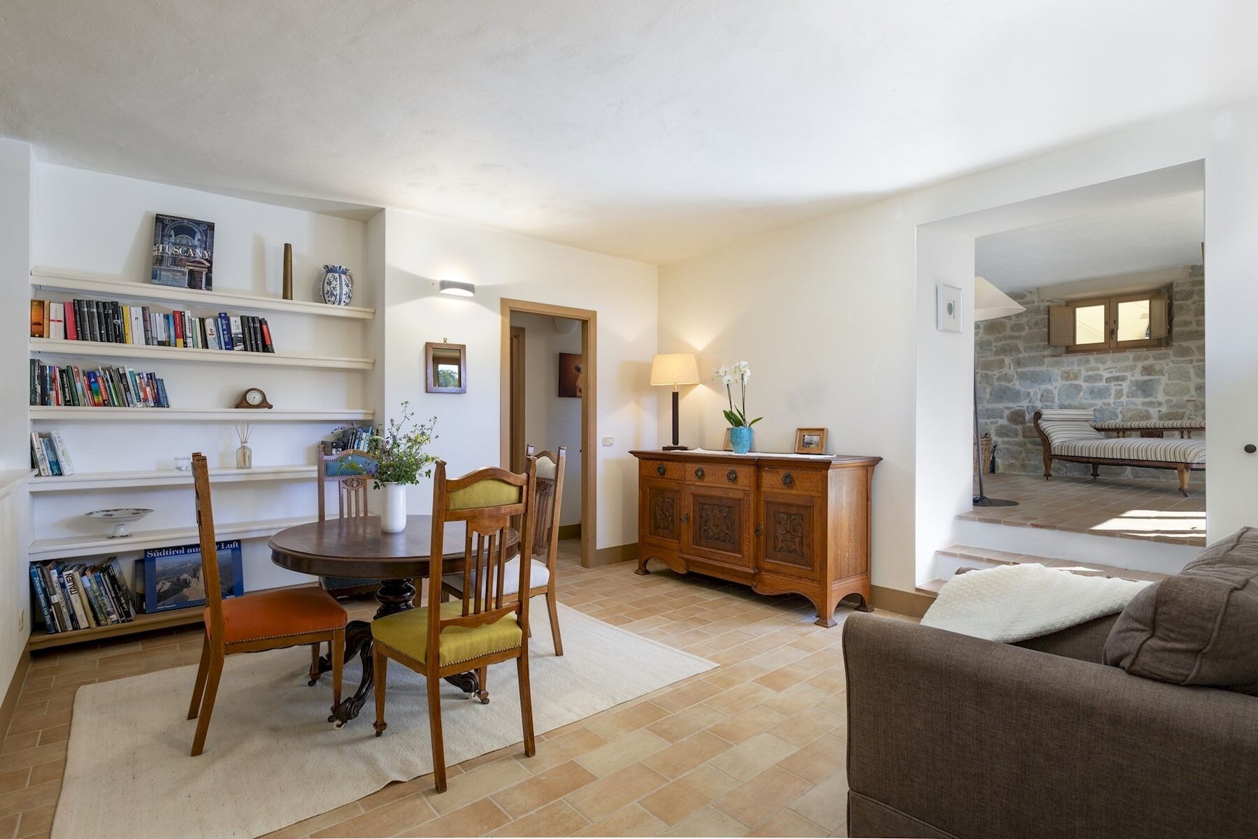 Una sala de estar acogedora con comedor, una estantería, un mueble de madera y una pared de piedra.