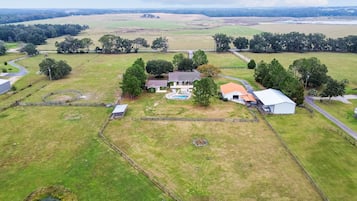 An aerial view of a rural property with a large house, a swimming pool, and fenced areas.