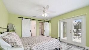 Ein Schlafzimmer mit Bett, Deckenventilator, Schiebeglasdoor zu einem Balkon und einem begehbaren Kleiderschrank.