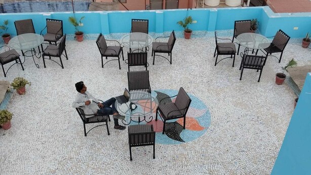 A rooftop patio with outdoor seating and a person using a laptop. - Fort view palace (Jodhpur)