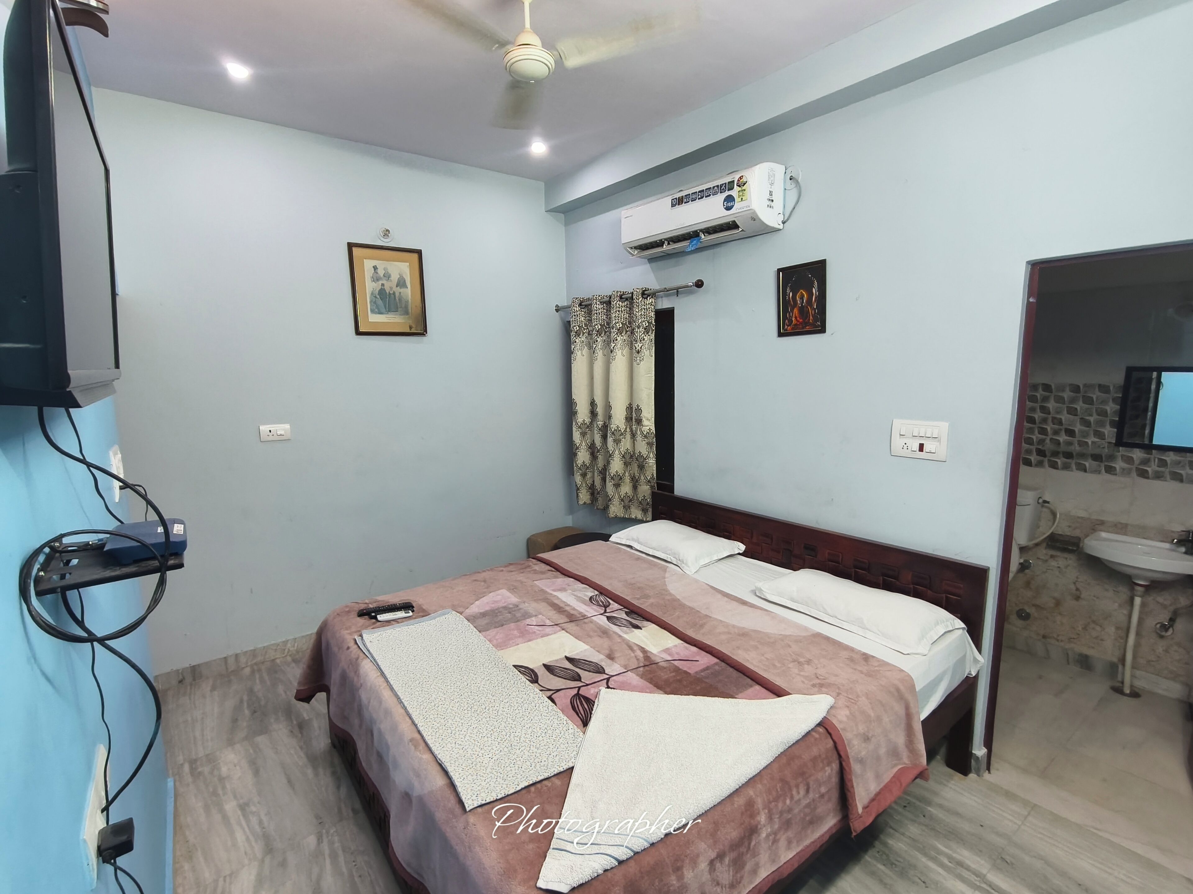 Una camera da letto con un letto, condizionatore, televisione e bagno visibile attraverso una porta aperta.