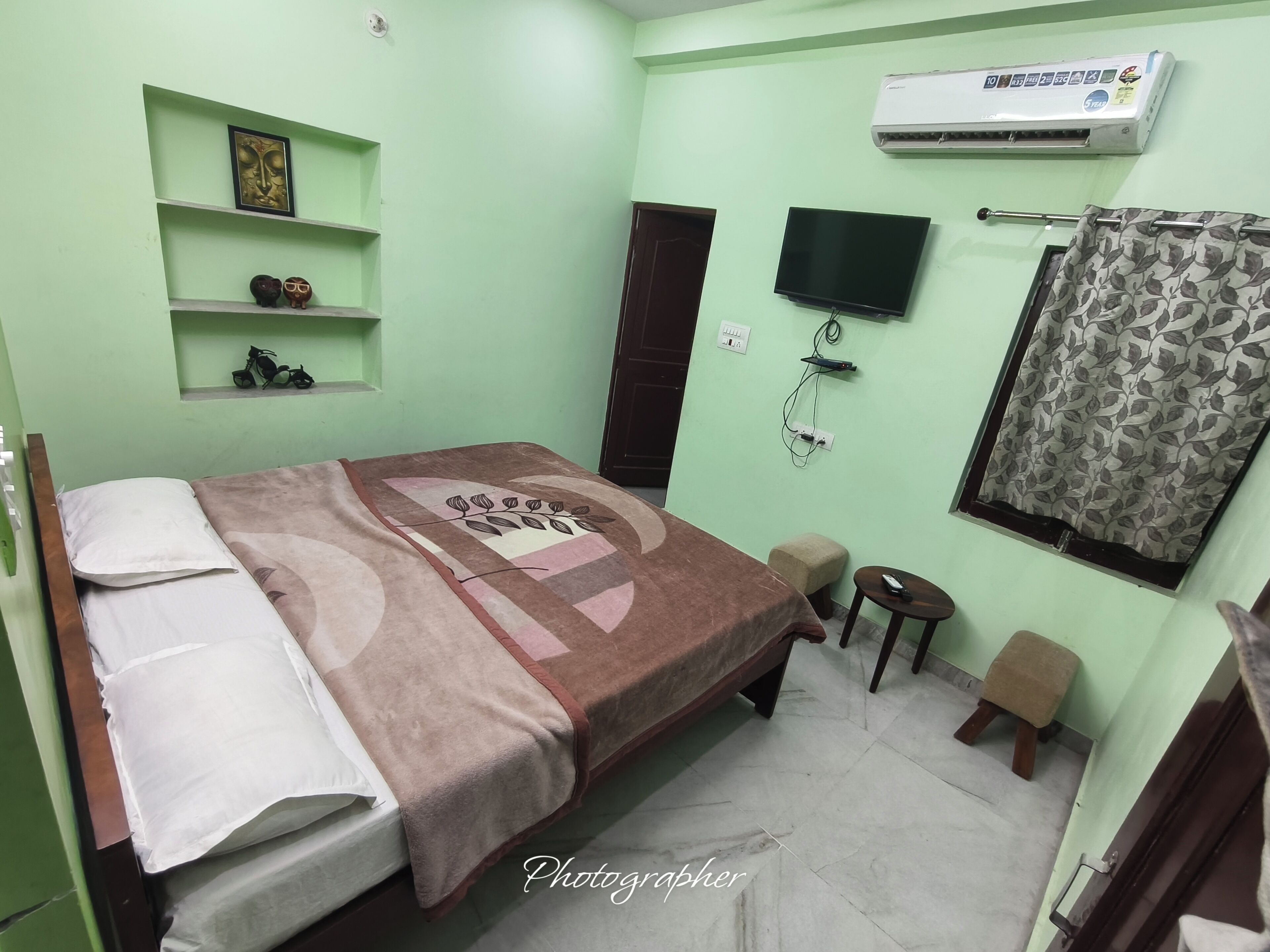 A room with a bed, a TV, an air conditioner, and a small table with a remote control.