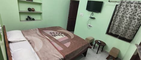 A room with a bed, a TV, an air conditioner, and a small table with a remote control.