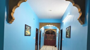 A hallway with blue walls, a marble floor, and a decorative archway leading to a door. - Fort view palace (Jodhpur)
