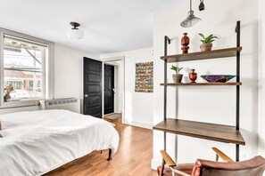 Ein Schlafzimmer mit einem Bett, Holzboden, einer schwarzen Tür, einem Fenster und einem Regal mit Dekoration.