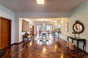 Un pasillo amplio con suelo de parquet de madera, un comedor con candelabro y un espejo grande en la pared derecha.