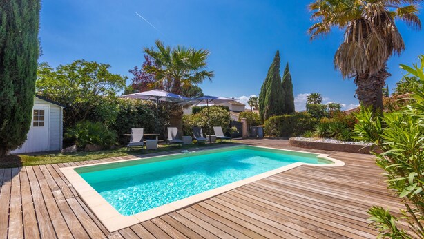 Una terraza de madera con piscina, rodeada de palmeras y un pequeño cobertizo.