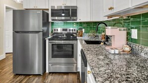 A modern kitchen with white cabinets, stainless steel appliances, a granite countertop, and a green backsplash. - Safety Harbor Motel (Safety Harbor)
