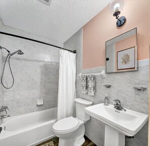 A bathroom with a bathtub, toilet, and sink, featuring marble tiles and a framed artwork on the wall. - Safety Harbor Motel (Safety Harbor)